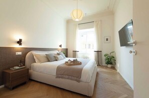 A hotel room with a bed, bedside table, lamp, TV, and a window with curtains. - New Listing (Roma)
