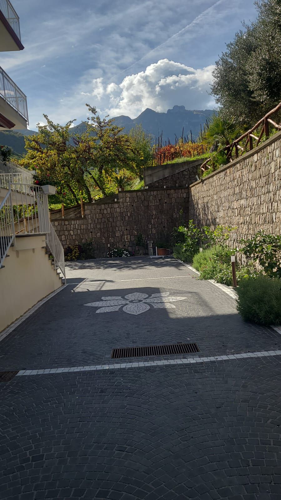 A paved courtyard with a stone wall, a metal staircase, and a view of mountains.