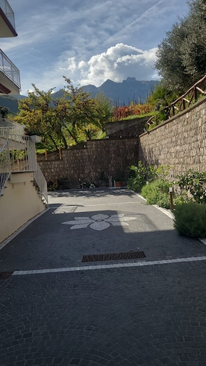 Un cortile pavimentato con un muro in pietra, una scala in metallo e vista sulle montagne.