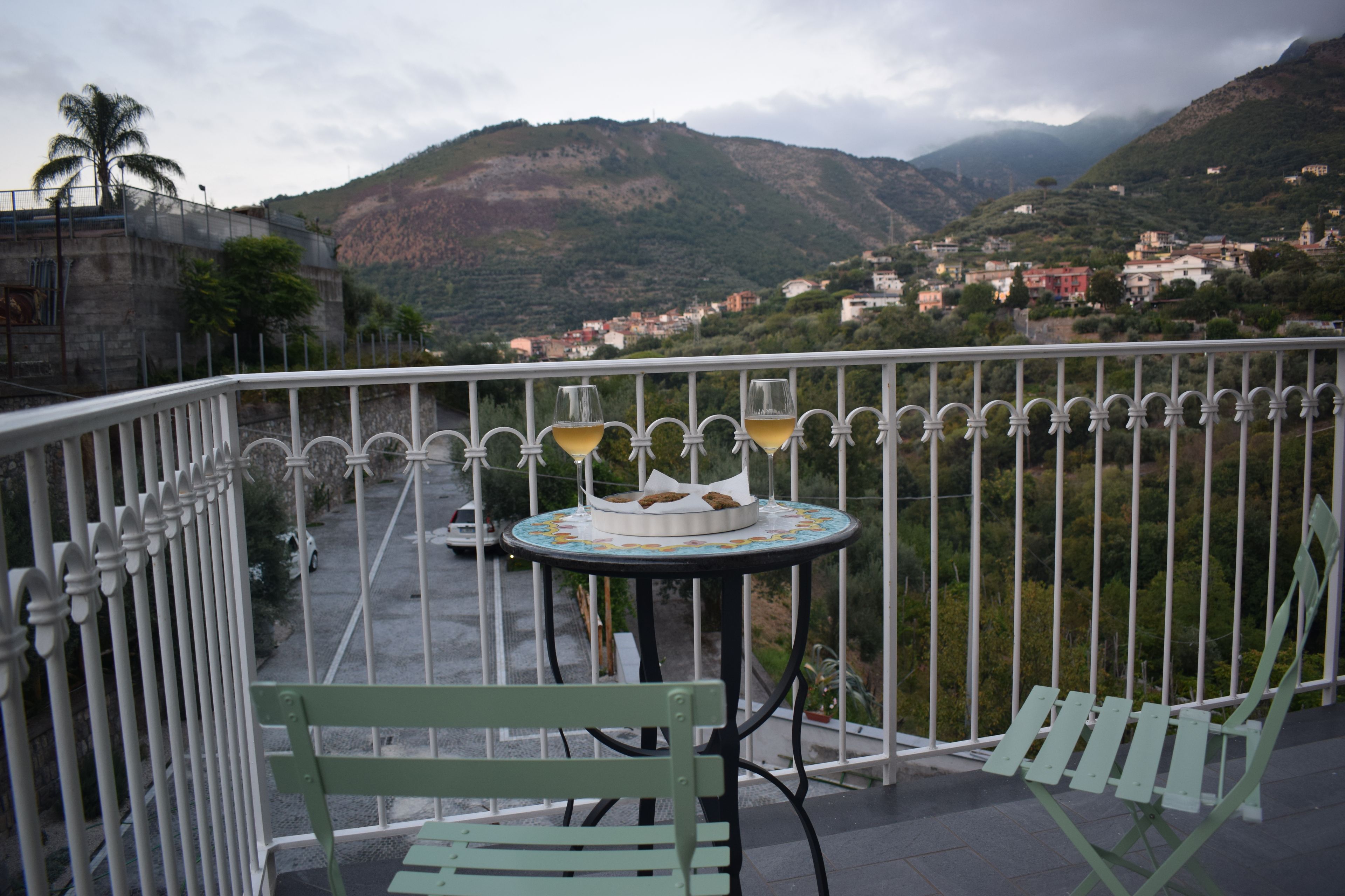 Un balcone con un tavolo, due sedie e un bicchiere di vino.