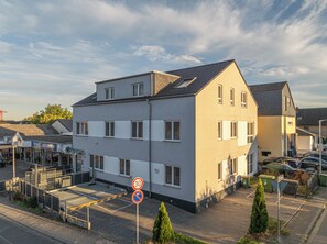A multi-story residential building with a flat roof, a parking area with cars, and a no parking sign. - New Listing (Mainz)