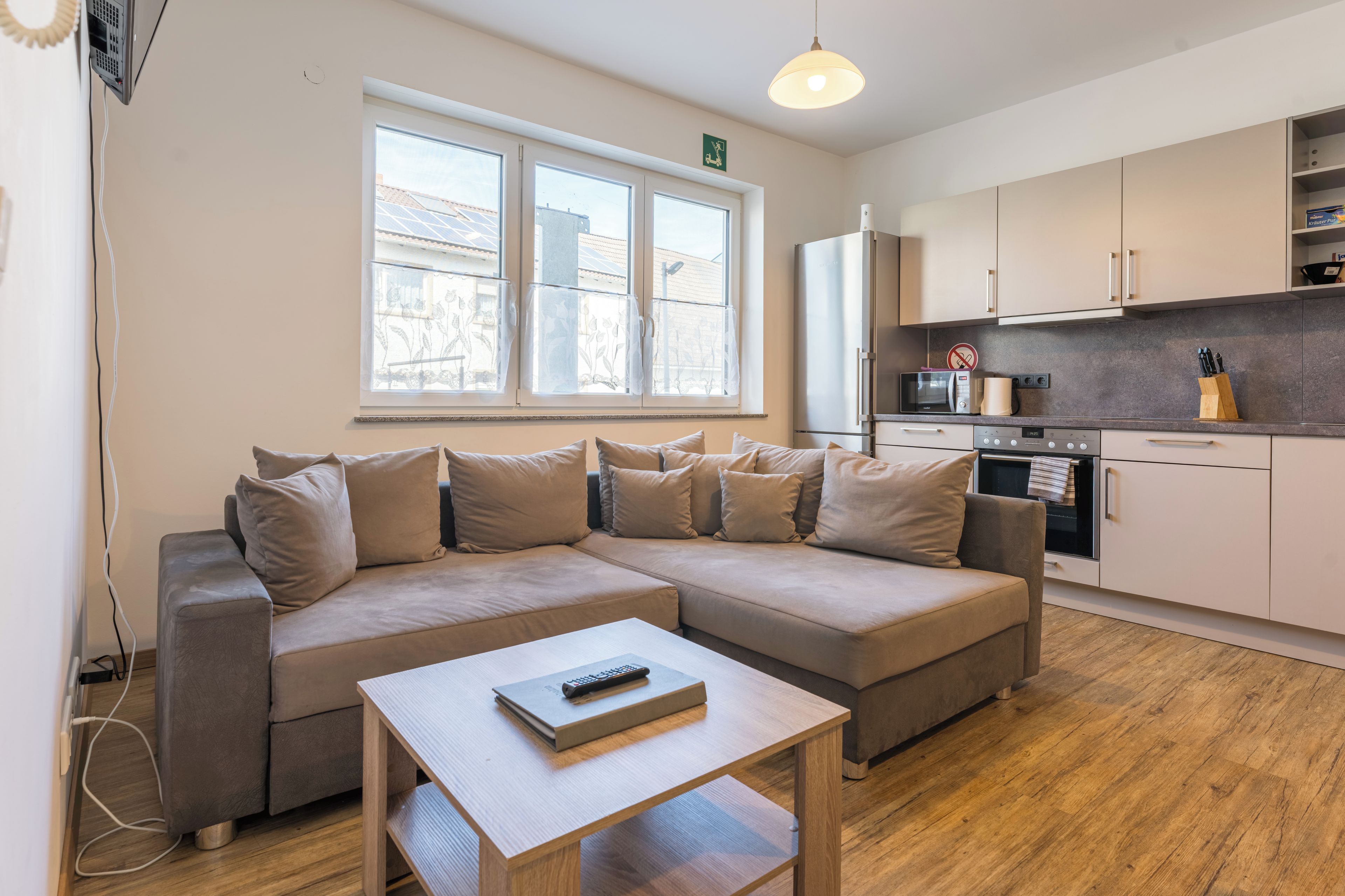A modern living room with a sectional sofa, a small table, and a kitchen area with appliances.