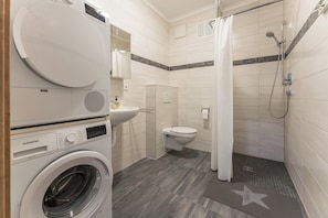 A compact bathroom with a washing machine, a toilet, and a shower area. - New Listing (Mainz)