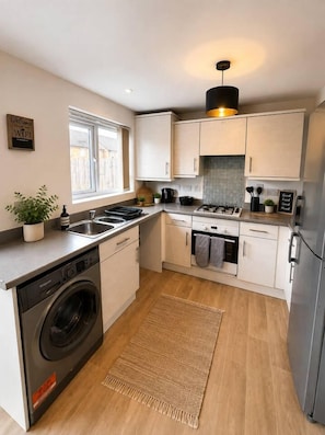 A compact kitchen with a washing machine, a stove, and a sink. - Prime Location Modern Home, Sleeps 5, Free Parking (Coventry)
