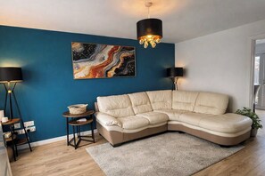 Een moderne woonkamer met een hoekbank, een blauwe accentmuur, een vloerlamp en een kroonluchter.