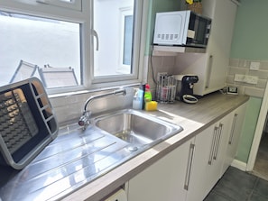 A kitchen with a stainless steel sink, a toaster, a microwave, and a coffee maker. - COSY STATION ESCAPE (Brighton and Hove)