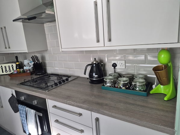 A kitchen with a gas stove, a kettle, and various kitchen utensils.
