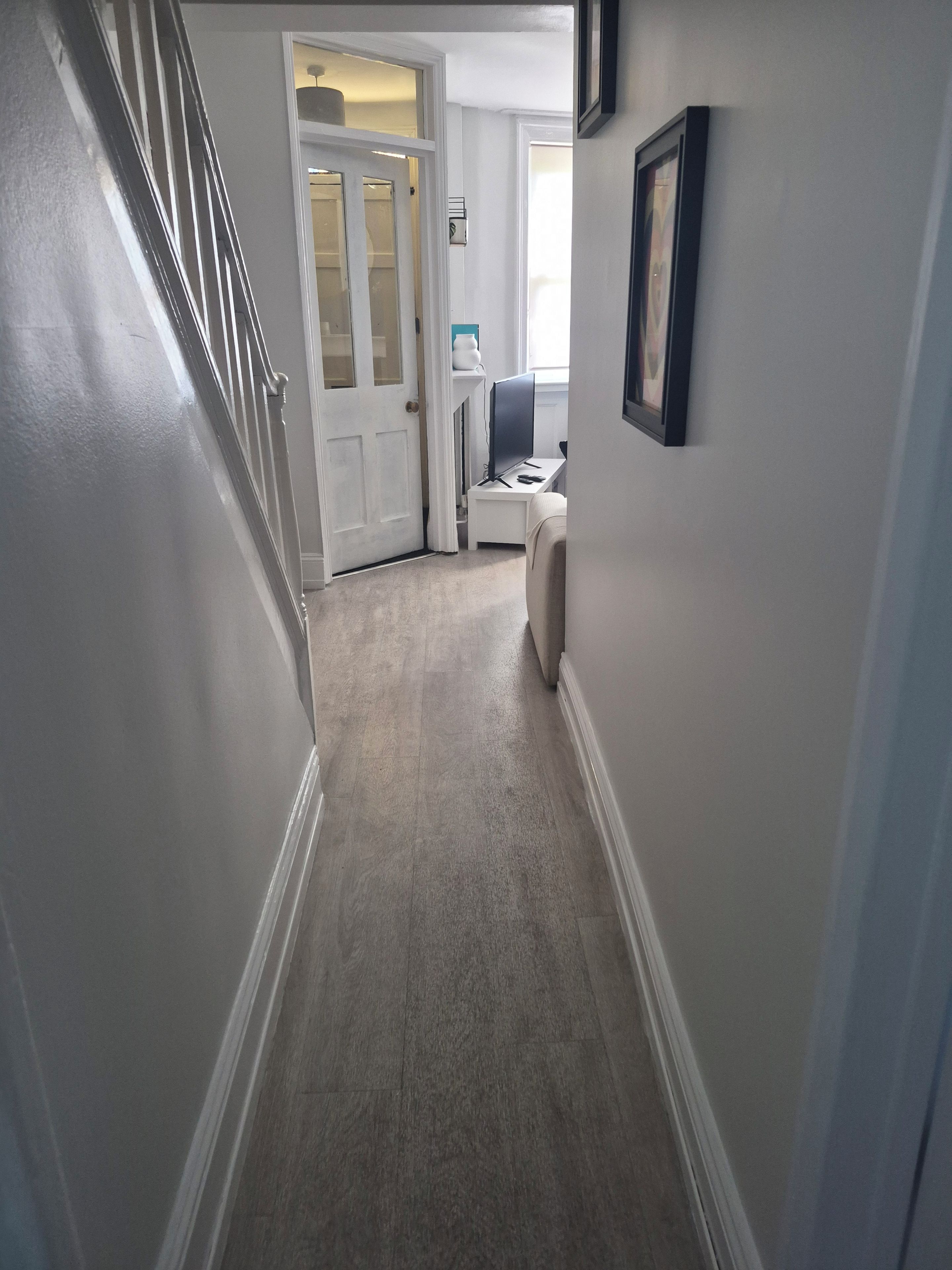 A hallway with a door leading to a room, a small table with a chair, and a framed picture on the wall.