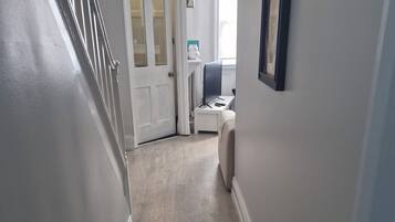 A hallway with a door leading to a room, a small table with a chair, and a framed picture on the wall.