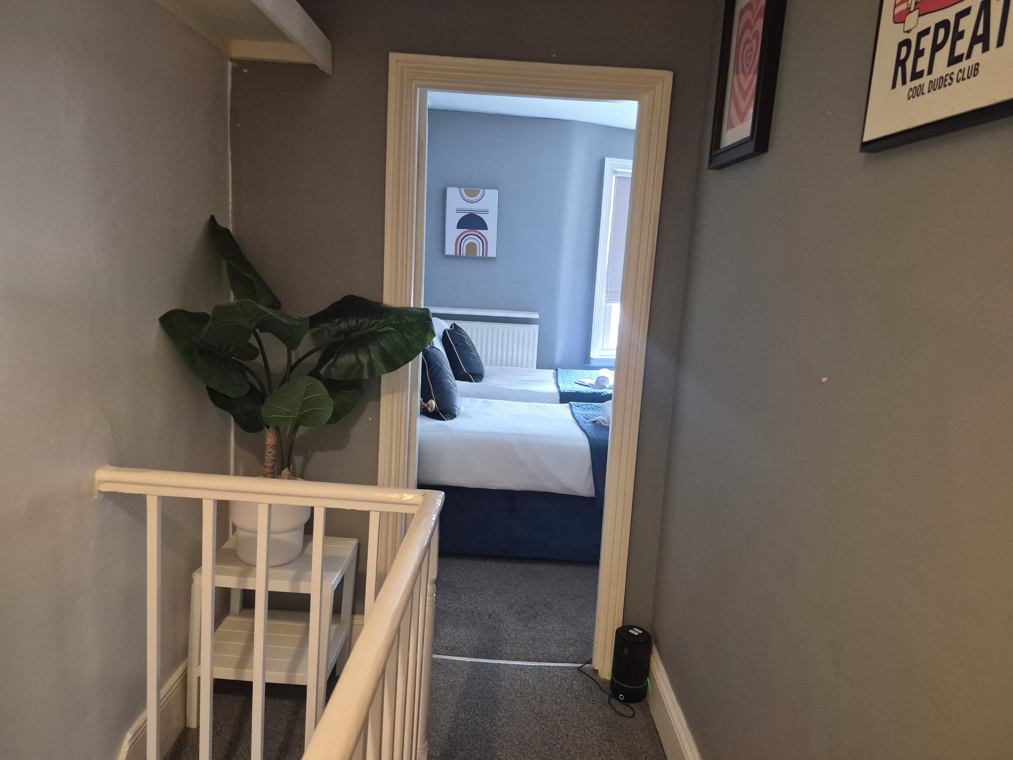 A hallway leading to a bedroom with a bed, a potted plant, and a framed picture on the wall.