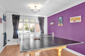 Ein Tischtennis-Tisch in einem Raum mit violetten Wänden, einem Fenster mit Vorhängen und zwei Bildern an der Wand.