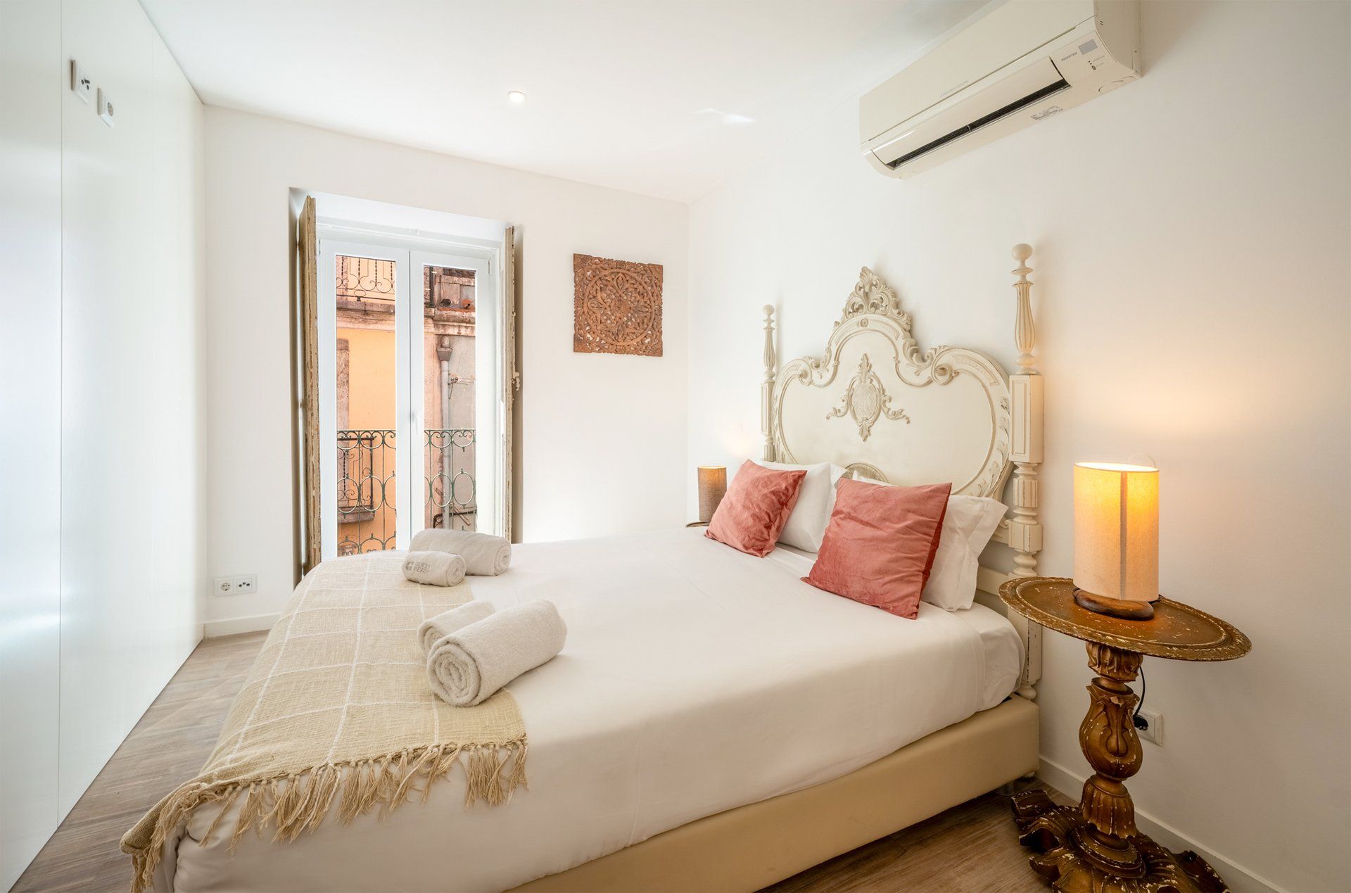 Un dormitorio con cama, mesita de noche, lámpara y vistas al exterior.