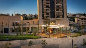 A playground with slides and swings, surrounded by a fence and a building with multiple floors. - Arnona Apartment - New & Modern WIth Private Mamad (Jerusalem)