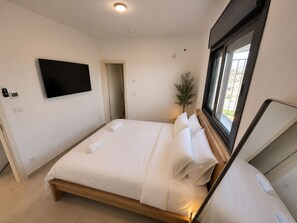 Ein modernes Schlafzimmer mit einem Bett, einem Flachbildfernseher, einer Topfpflanze und einem Fenster.