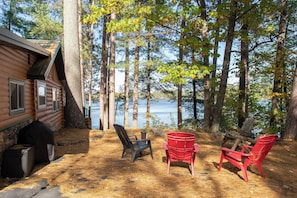 A cabin with a view of a lake, surrounded by tall trees and equipped with outdoor seating. - Cozy log cabin on George Lake in Rhinelander, Wisconsin. (Rhinelander)