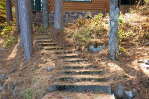 A wooden cabin with a stone foundation, surrounded by trees and a wooden deck. - Cozy log cabin on George Lake in Rhinelander, Wisconsin. (Rhinelander)