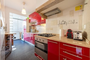 A modern kitchen with red cabinetry, a gas stove, a coffee maker, and a microwave. - GuestReady - Cozy 3-Bedroom Apartment with Terrace (Lisbon)