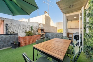 An outdoor patio with a wooden table and chairs, a barbecue grill, and a green umbrella. - GuestReady - Cozy 3-Bedroom Apartment with Terrace (Lisbon)