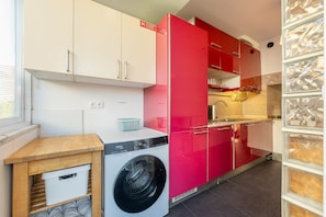 Une petite cuisine équipée d’un lave-linge, d’un évier et d’une fenêtre.