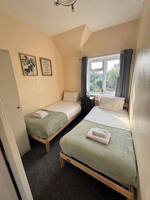 A small, cozy room with two single beds, a window with curtains, and a door. - Central Property with Free Parking, Sleeps 6 (Warwickshire)