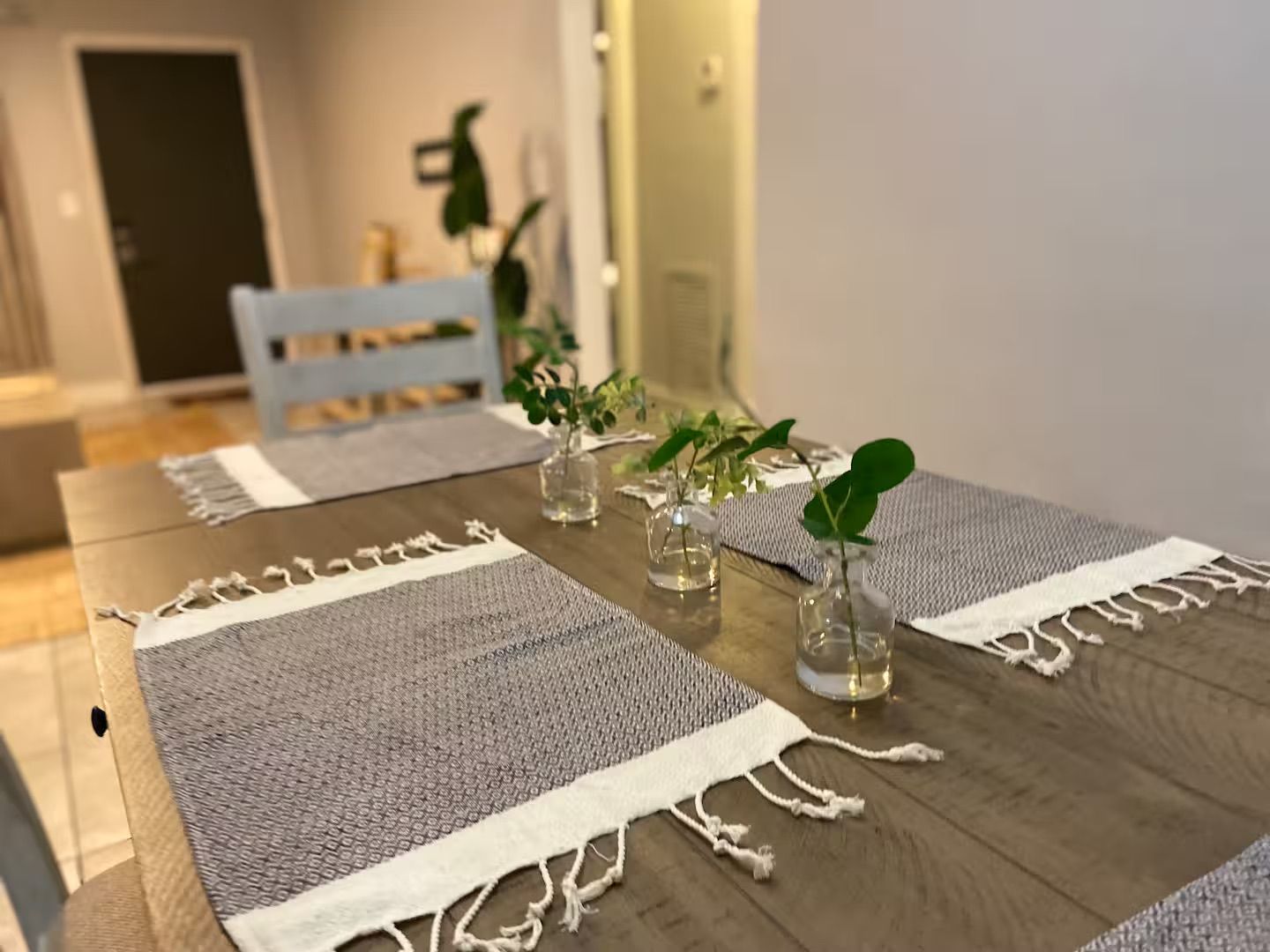 A wooden dining table with a woven placemat and small glass vases with plants.