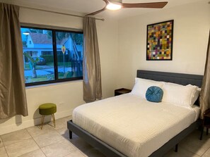 A bedroom with a bed, a nightstand, a window with curtains, a ceiling fan, and a wall art piece. - Modern 4-bedroom Oasis in North Miami w/ HOT TUB (Miami)
