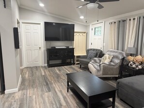 Un salon moderne avec un téléviseur à écran plat, un fauteuil gris, une table basse noire et un plancher en bois.