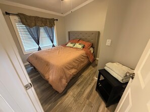 Une chambre à coucher avec un lit, une table de chevet, une fenêtre avec des rideaux et une porte.