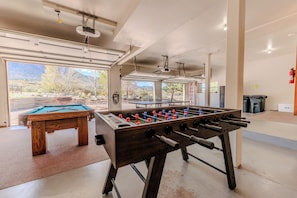 A spacious indoor area with a foosball table, a pool table, and a view of a mountainous landscape through large windows. - Mountain Views - Hot Tub Two Game Rooms (Monument)