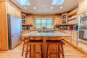 A kitchen with wooden cabinets, a central island with stools, a refrigerator, and a microwave. - Mountain Views - Hot Tub Two Game Rooms (Monument)