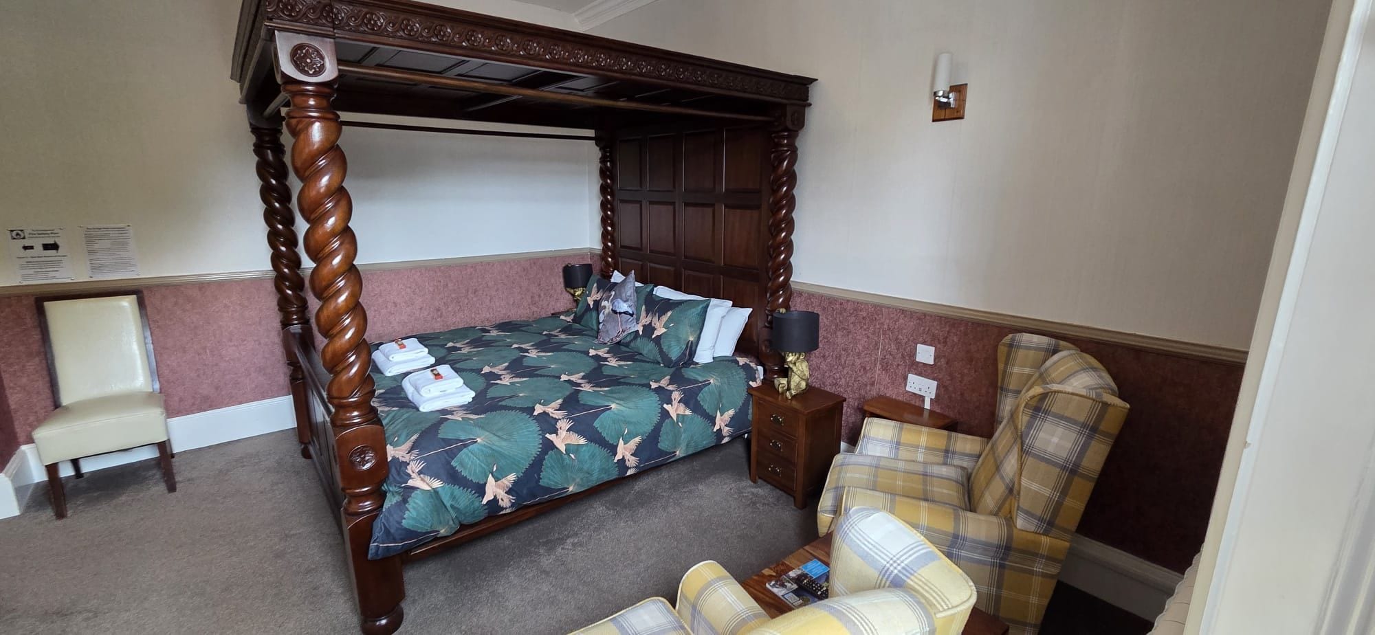 A bedroom with a four-poster bed, a chair, a small table, and a lamp.
