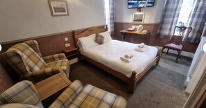 A hotel room with a bed, a chair, a bedside table, a television, and a window with curtains. - The Roy Bridge Hotel (Roybridge)