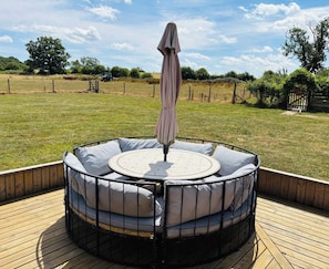 A round outdoor seating area with a table and chairs, surrounded by a wooden deck. - Woodland Forge - The Stables (Over Whitacre)