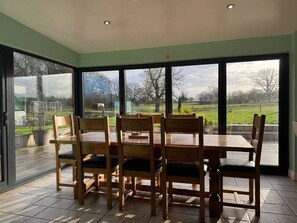 A dining area with a table and chairs, large windows, and a view of the outdoors. - Woodland Forge - The Stables (Over Whitacre)
