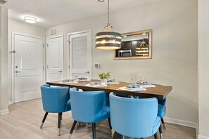 Un coin repas avec une table en bois, quatre chaises bleues, une suspension et un miroir fixé au mur.