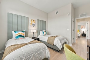 A hotel room with two beds, a bedside table with a lamp, a chair, and a door leading to another room. - Vista Cay 3BR Condo Pools Near Universal (Orlando)