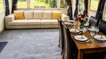 A dining area with a wooden table set for four, a sofa, and a view of greenery outside.