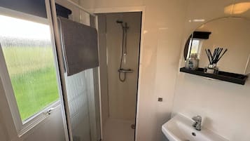 Une salle de bain avec une douche, un lavabo et une fenêtre donnant sur un espace verdoyant.