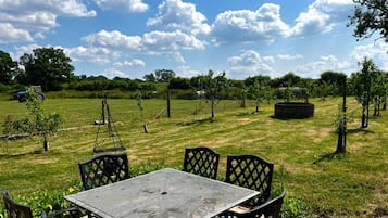 An outdoor seating area with a table and chairs, surrounded by a grassy field and trees.