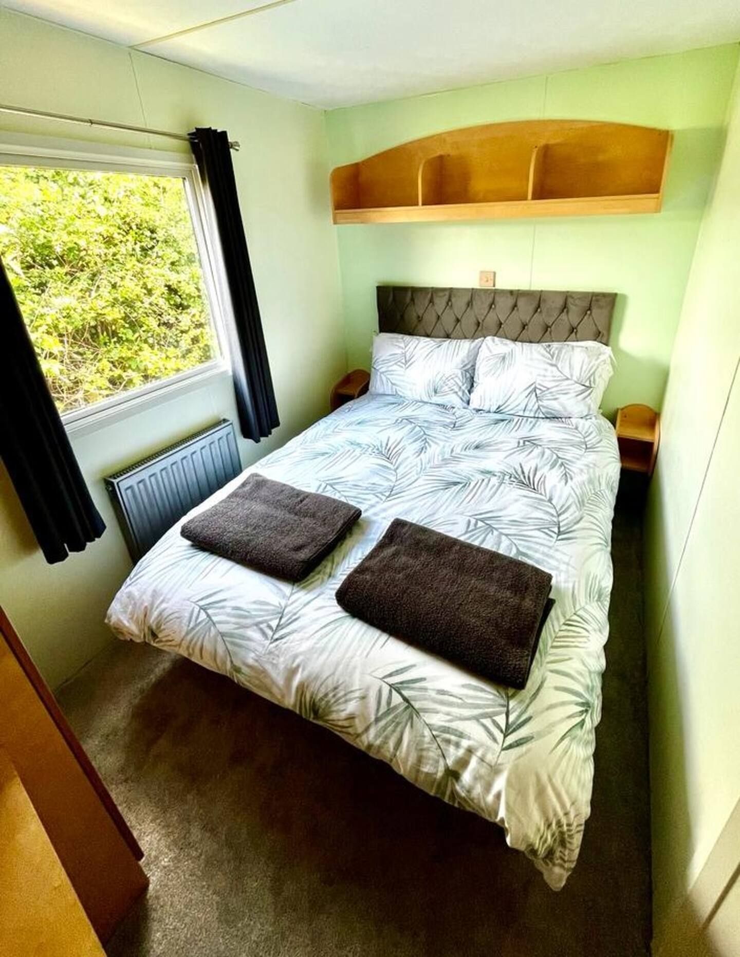 A bedroom with a bed, a window with curtains, a radiator, and a headboard.