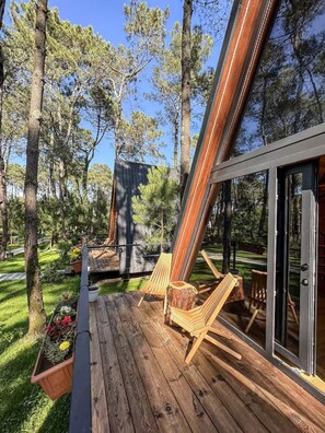 Une terrasse avec un plancher en bois, deux chaises en bois et une porte vitrée donnant sur un espace abrité.