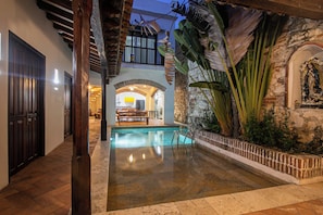 Zona de piscina con suelo de piedra, rodeada de un muro de ladrillo y plantas tropicales.