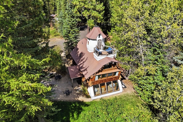 Eine zweistöckige Holzhütte mit Balkon, umgeben von dichtem Wald.