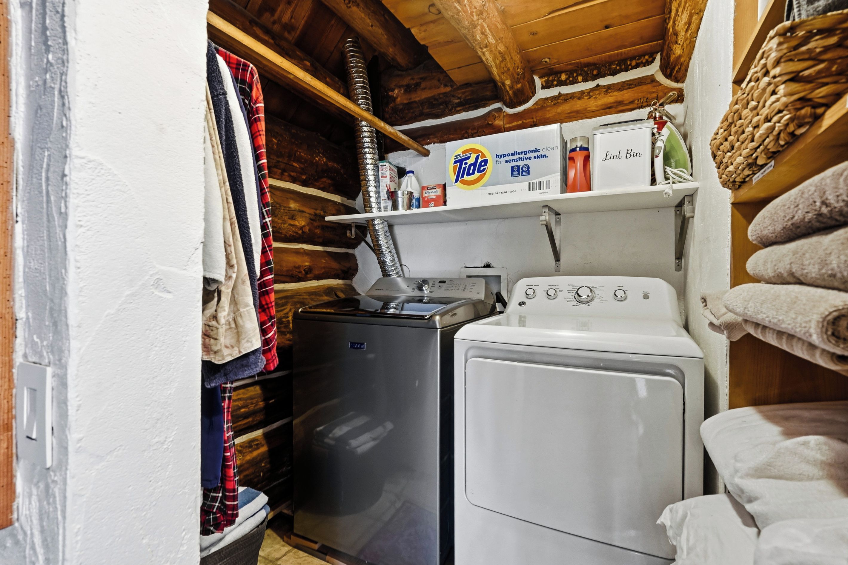 A compact laundry area with a washing machine and dryer, a small heater, and a shelf with cleaning supplies.