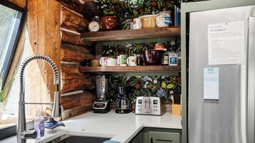 A compact kitchen with wooden shelves, a coffee maker, a blender, and a refrigerator.