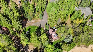 An aerial view of a residential area with a house surrounded by dense trees, a visible driveway, and a small swimming pool.