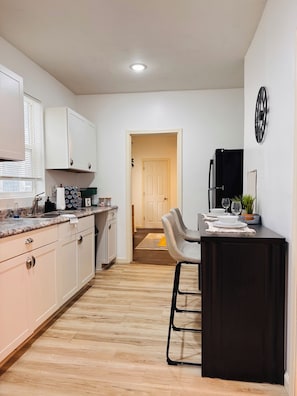A compact kitchen with white cabinets, a black refrigerator, and a dining area with a bar stool. - Furnished Extended Stay Near Downtown Indy (Indianapolis)