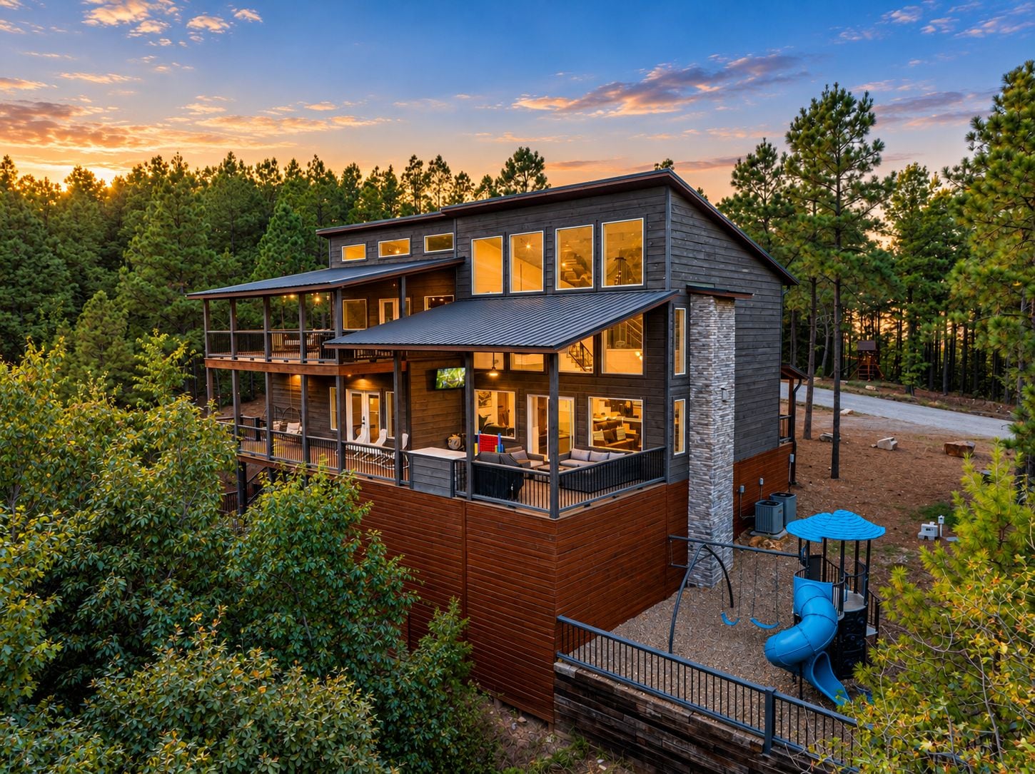 A modern multi-story house with a balcony, surrounded by dense forest.