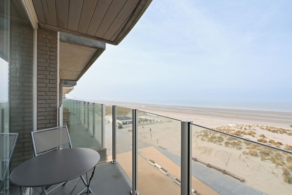 Un balcon avec vue sur la plage, une table et des chaises.