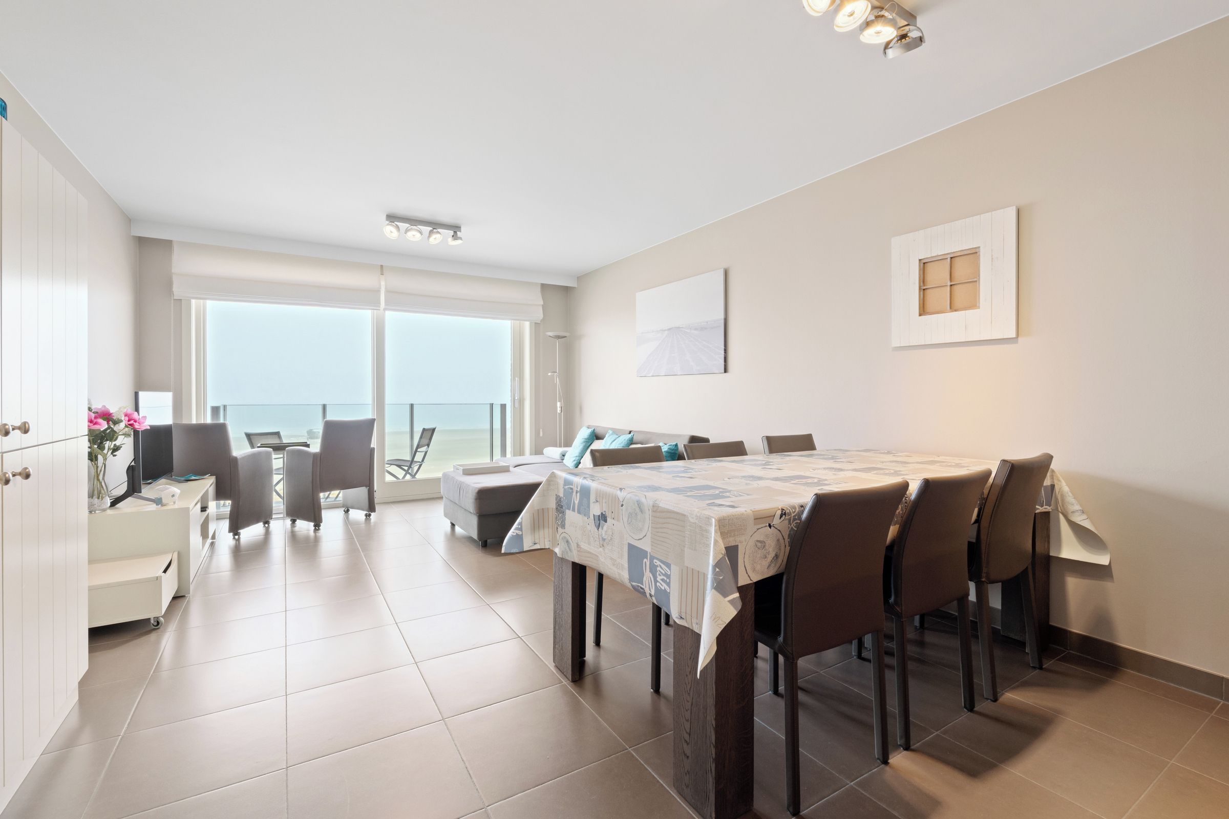 A spacious dining area with a large table and chairs, a balcony with a view, and a modern kitchen area.